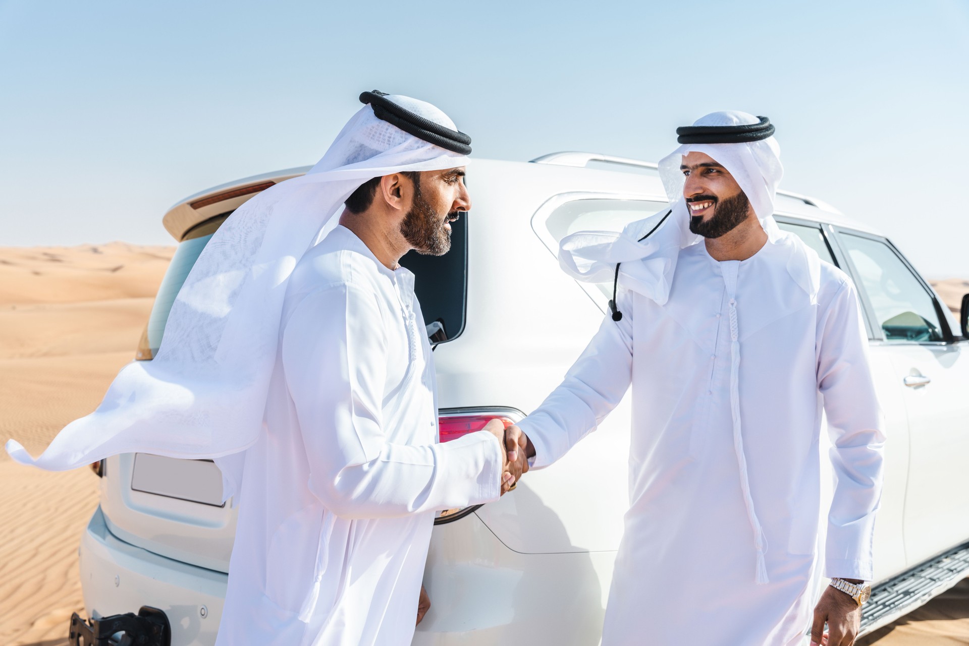 Two middle-eastern emirati men wearing arab kandura driving car in the desert